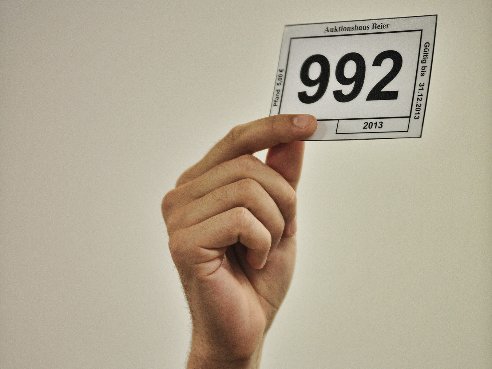 Eine Hand hält einen Nummerzettel hoch, der bei der Versteigerung der nicht abgeholten Fundsachen des BVG Fundbüros genutzt wird, um etwas zu ersteigern
