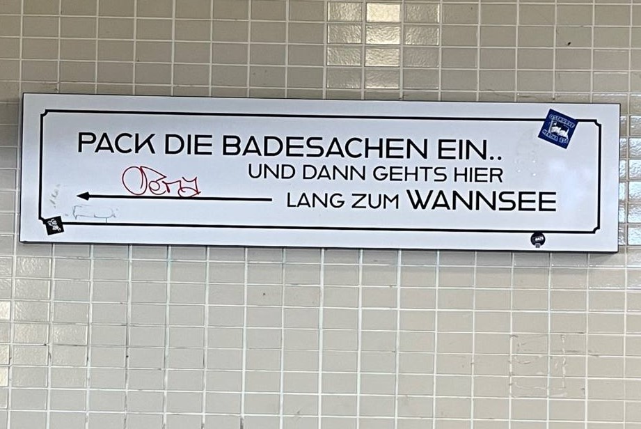 Eine Fliese im S-Bahnhof Nikolassee mit der Aufschrift "Pack die Badesachen ein. Und dann gehts hier lang zum Wannsee"